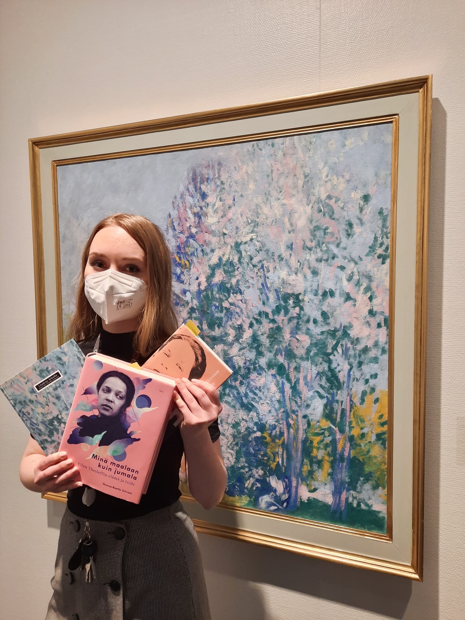 nainen pitelee kädessään kirjoja taustanaan Ellen Thesleffin maalaus Ihmisiä luonnossa.