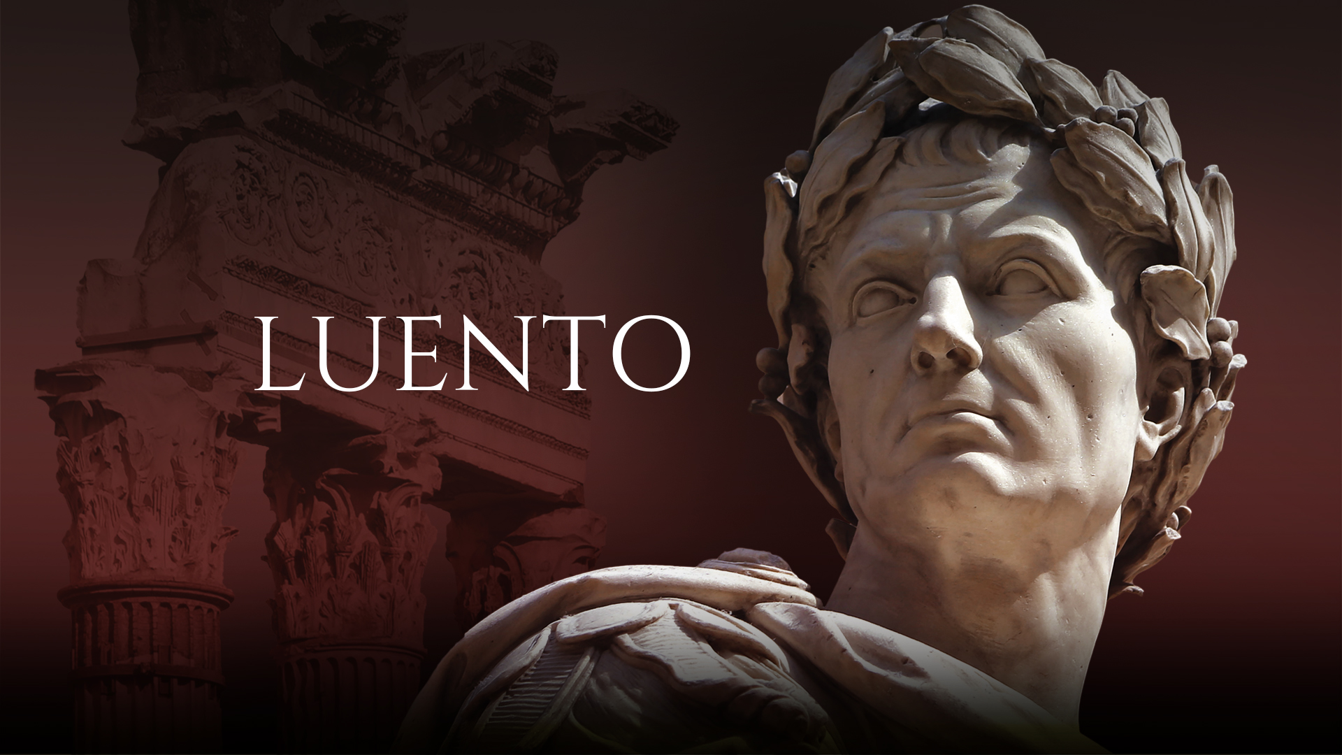 Marmoripatsas, joka esittää Julius Caesaria laakerinlehtiseppele päässä. Teksti "LUENTO".