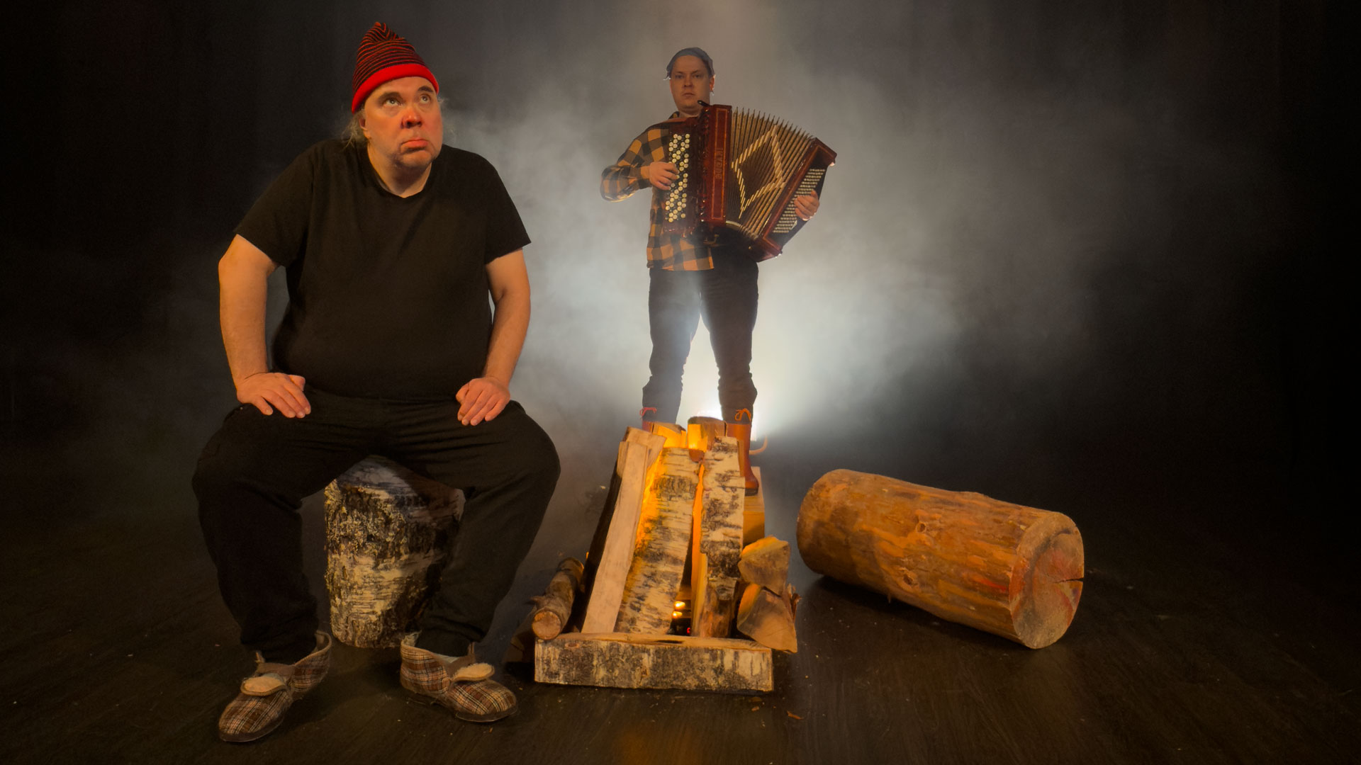 kaksii miestä tummalla, usvaisella taustalla. Toisella on haitari