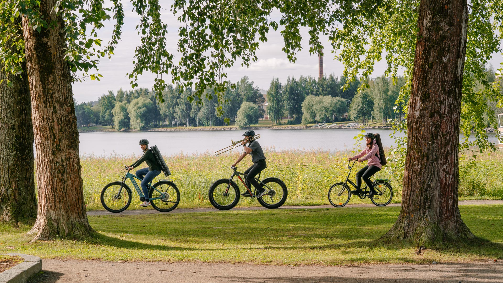orkesterin jäseniä pyöräilemässä järvimaisemassa soitinten kanssa